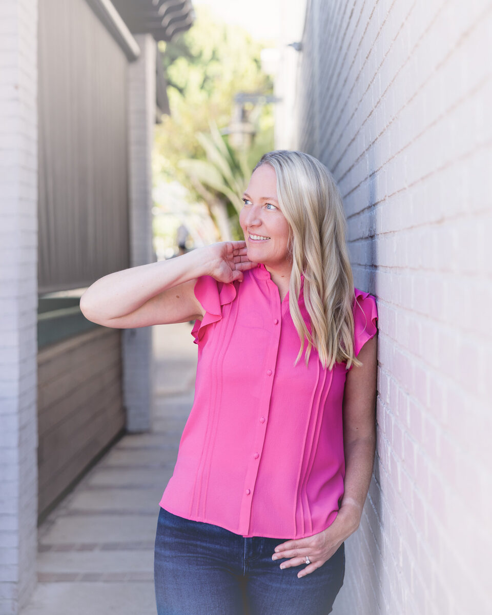 Christine Glover leaning against a brick wall in a fuchsia blouse, smiling